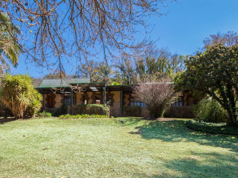 A view of the rear exterior of the farm property, featuring a covered patio area, stone-accented facade, and a spacious lawn.