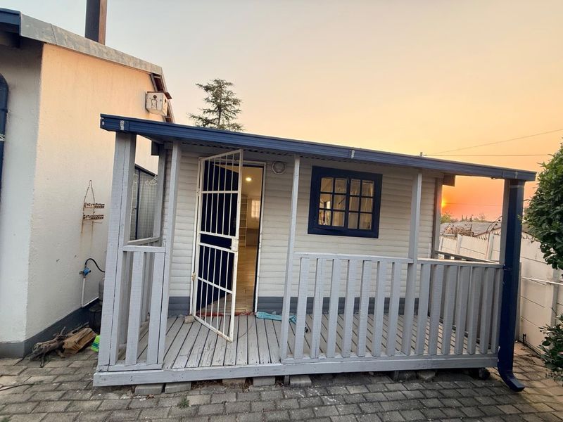 A rear view of a timber cottage featuring a covered deck, security gate, and painted timber cladding at sunset.
