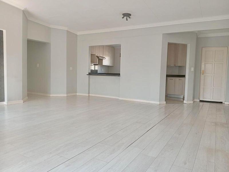 Spacious open-plan living area featuring light-toned laminate flooring, coved cornicing, and a convenient pass-through window connecting to the kitchen.