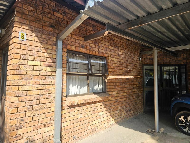 Front exterior view of the property featuring a face brick facade, a corrugated metal carport, and secure entrance access.