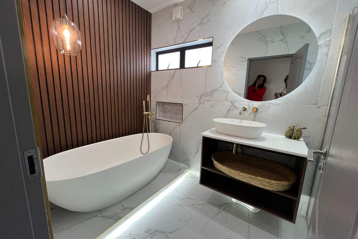 Modern bathroom featuring a freestanding bathtub, wall-mounted vanity with vessel sink, marble-look tiling, and decorative timber slat feature wall with integrated lighting.