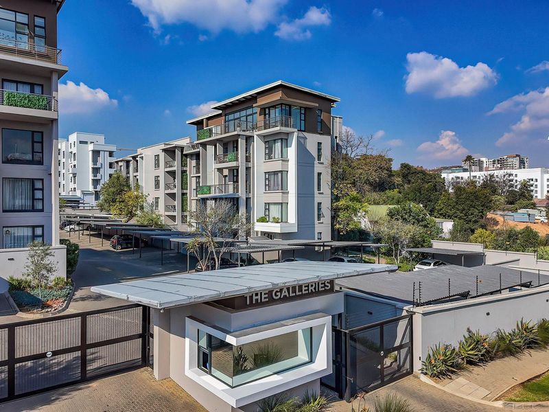 Aerial view of The Galleries apartment complex, featuring a secure gated entrance, covered parking facilities, and modern multi-story residential buildings.