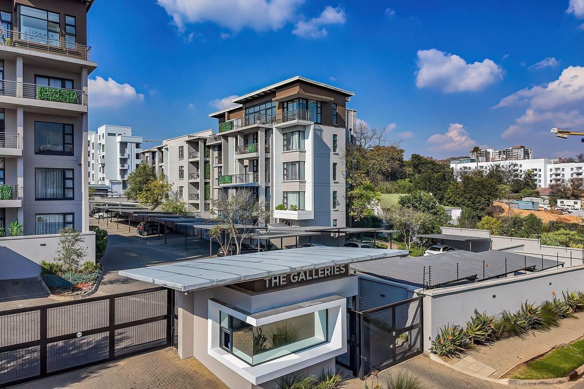 Aerial view of The Galleries apartment complex, featuring a secure gated entrance, covered parking facilities, and modern multi-story residential buildings.