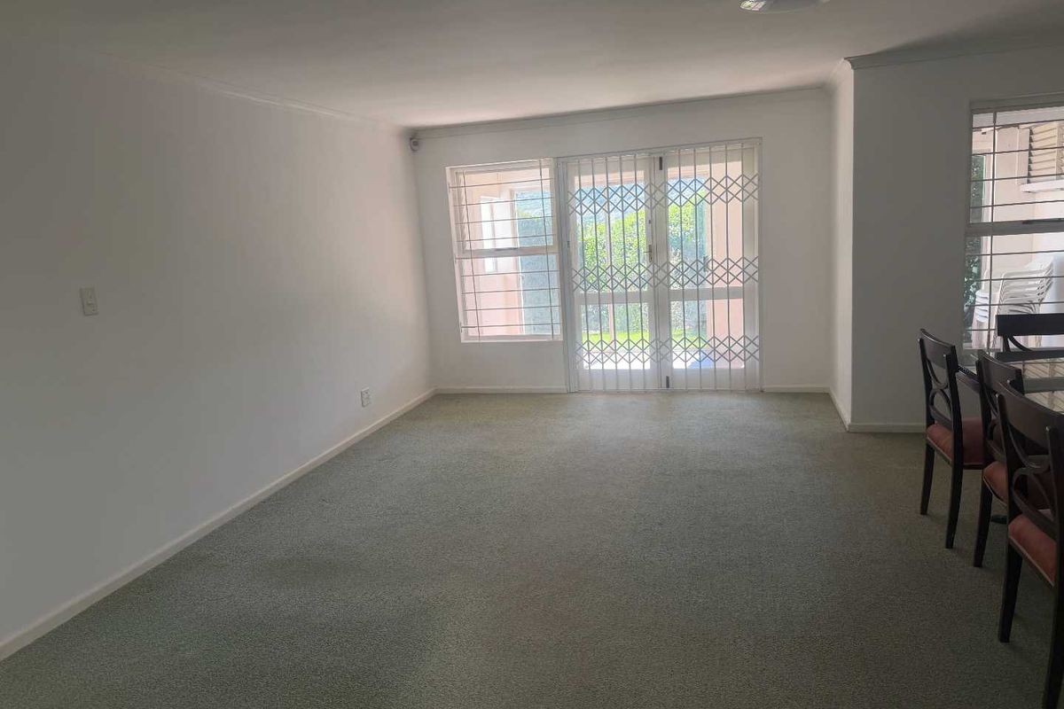 A spacious living area featuring neutral walls, carpeted flooring, and a security-gated sliding door providing access to the exterior.