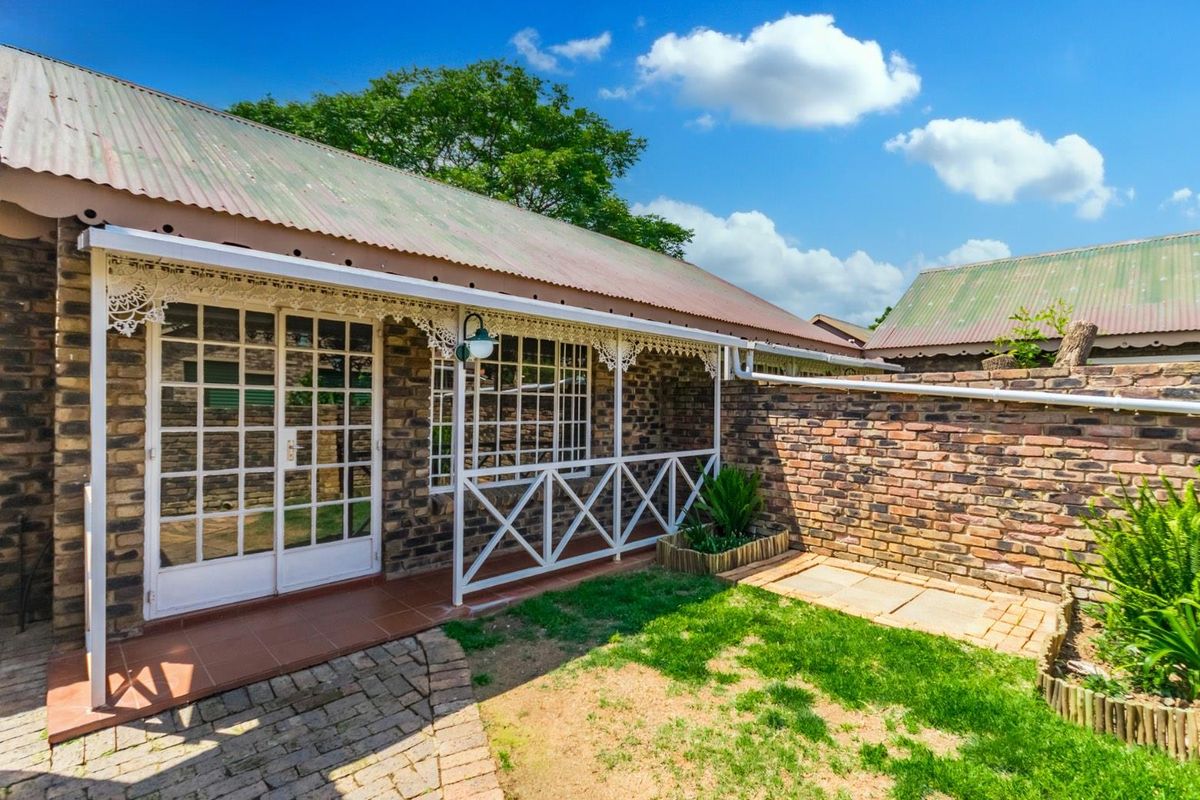 Rear exterior view of a townhouse featuring a covered patio with decorative ironwork, brick facade, and a private garden area.