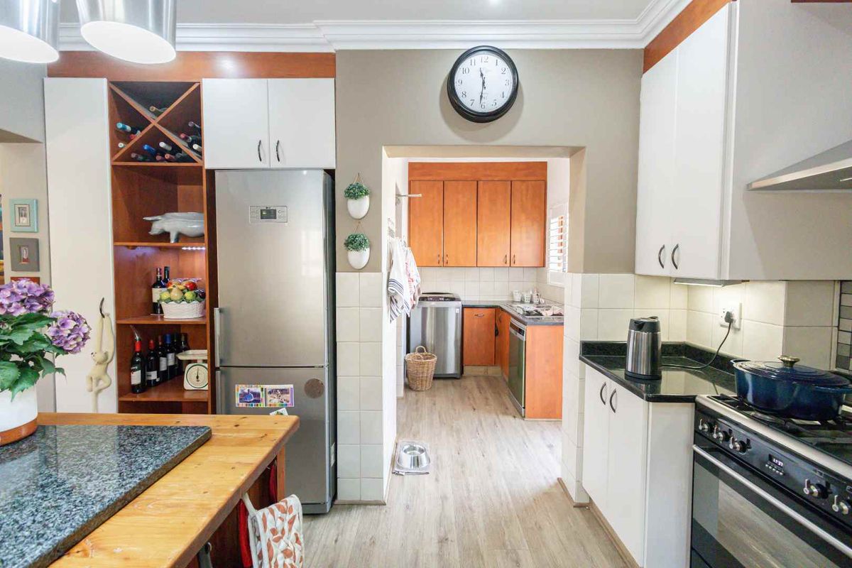 A functional kitchen featuring a mix of white and wood-toned cabinetry, granite countertops, and an adjoining scullery area with additional storage and workspace.