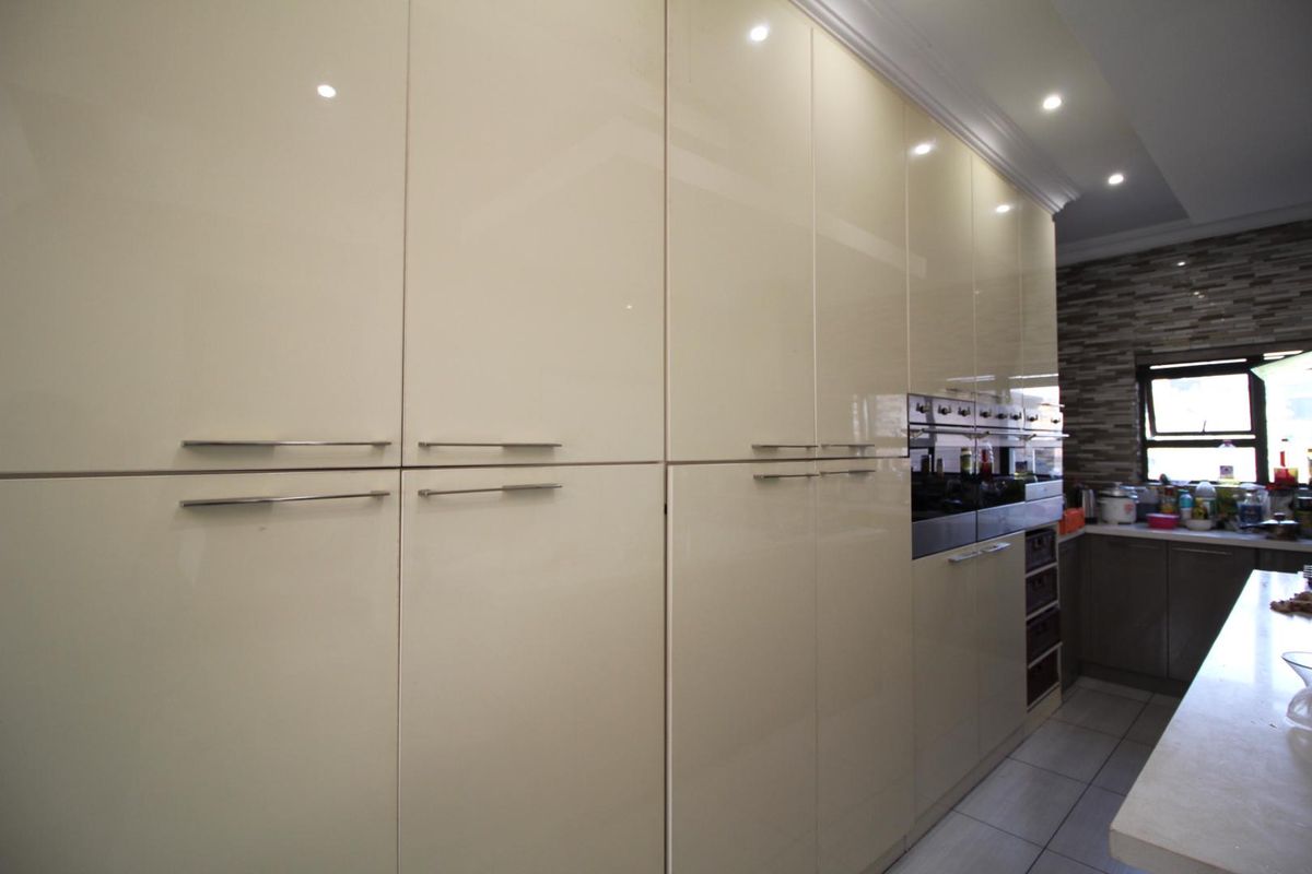 Modern kitchen featuring high-gloss cream cabinetry, integrated oven, and tiled flooring with a stone-tiled backsplash.