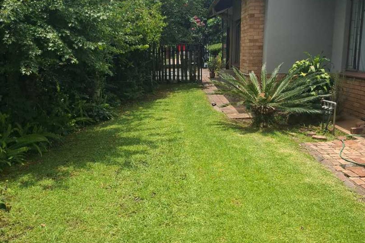 A view of the rear garden featuring a well-maintained lawn, brick chimney, and paved walkway leading to a timber gate.