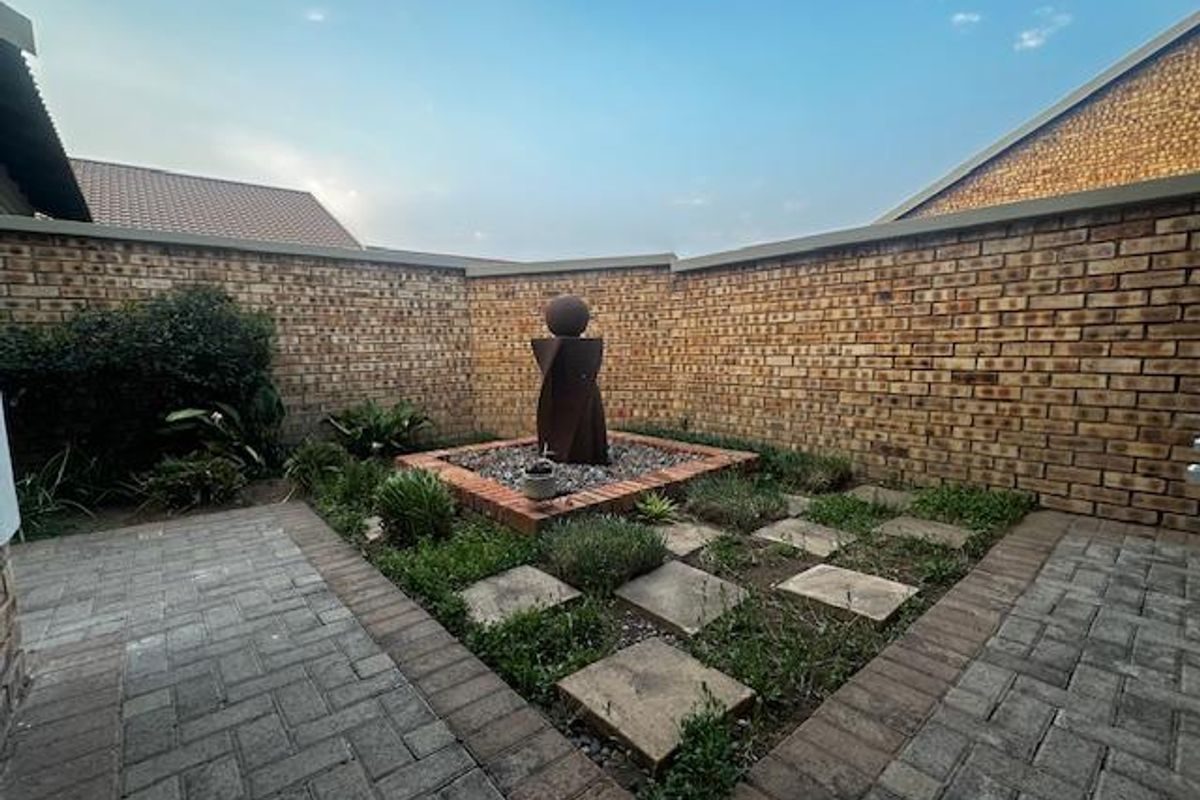 A private rear courtyard featuring brick boundary walls, paved walkways, and a central landscaped garden bed with a decorative water feature.