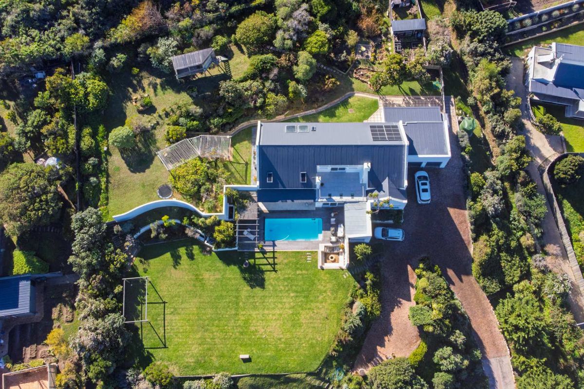 Aerial view of a residential property featuring a swimming pool, landscaped garden, solar panels, and a paved driveway.