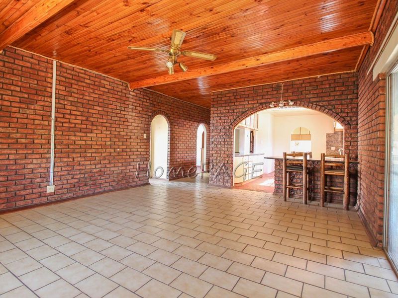 Spacious open-plan living area featuring exposed brick walls, timber ceiling, and ceramic floor tiles, with an arched transition to the kitchen area.