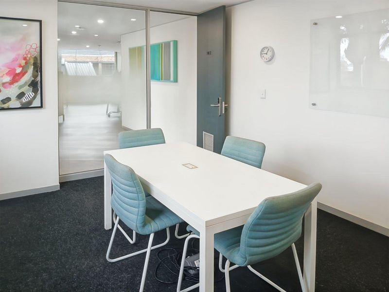A modern office meeting room featuring a glass partition wall, recessed lighting, and a wall-mounted glass whiteboard, providing a professional and bright workspace.
