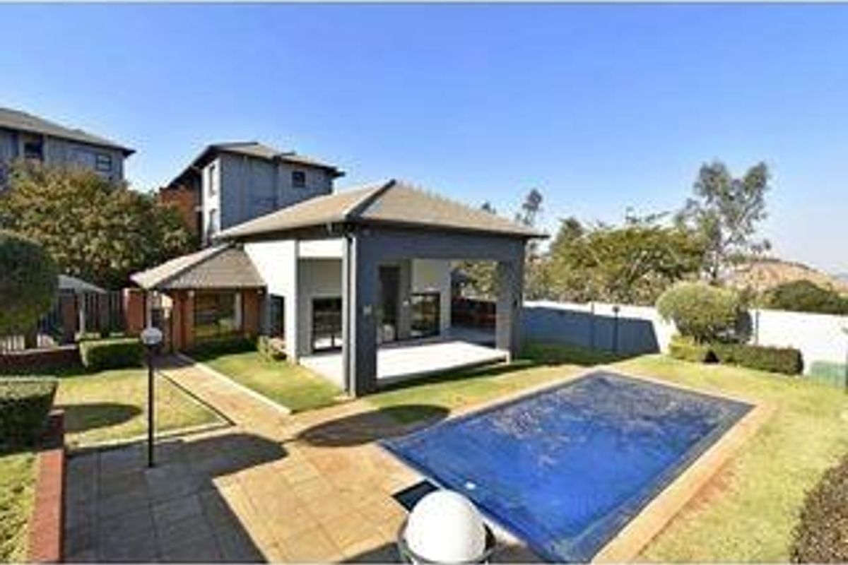 A rear view of the townhouse featuring a covered patio, a private swimming pool, and a landscaped garden area.