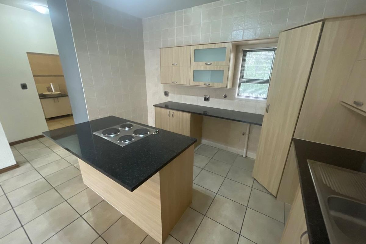 A functional kitchen featuring light wood cabinetry, dark granite countertops, a central island with an electric hob, and tiled flooring throughout.