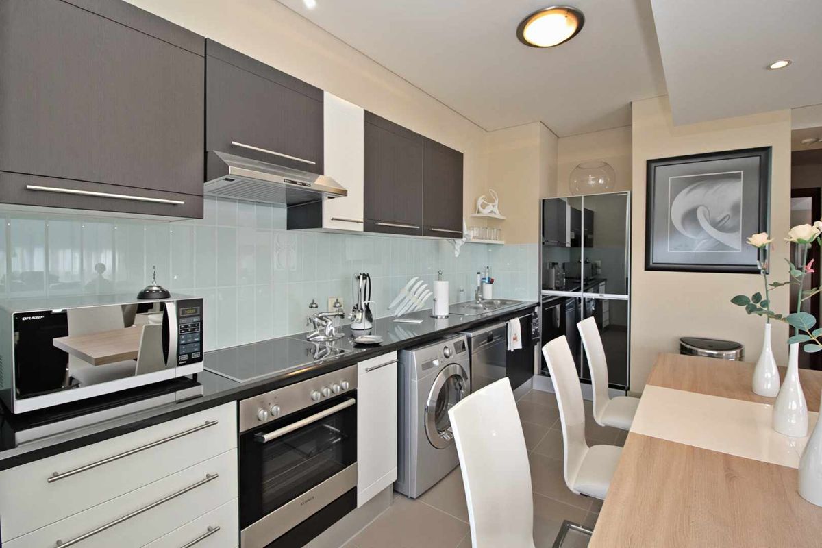 Modern kitchen featuring dark and white cabinetry, integrated appliances, sleek countertops, and a glass tile backsplash, seamlessly flowing into the dining area.
