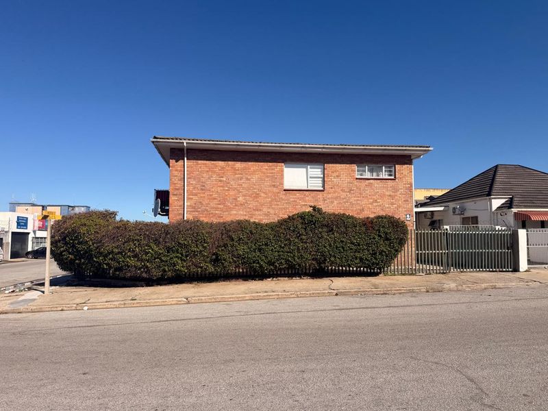Street view of a face brick apartment building featuring security fencing and established hedging along the front boundary.