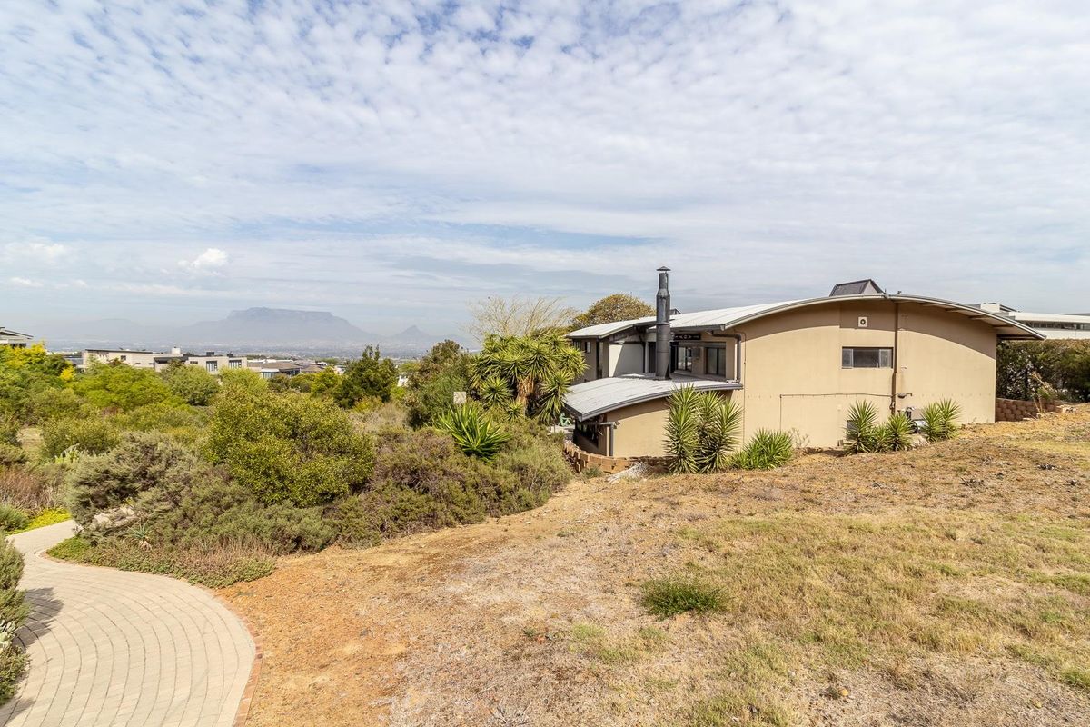Rear view of the property featuring a curved roofline, external chimney, and a paved walkway set against a scenic mountain backdrop.