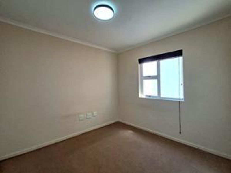 A clean, empty bedroom featuring neutral walls, carpeted flooring, and a functional sliding window with a fitted blind.