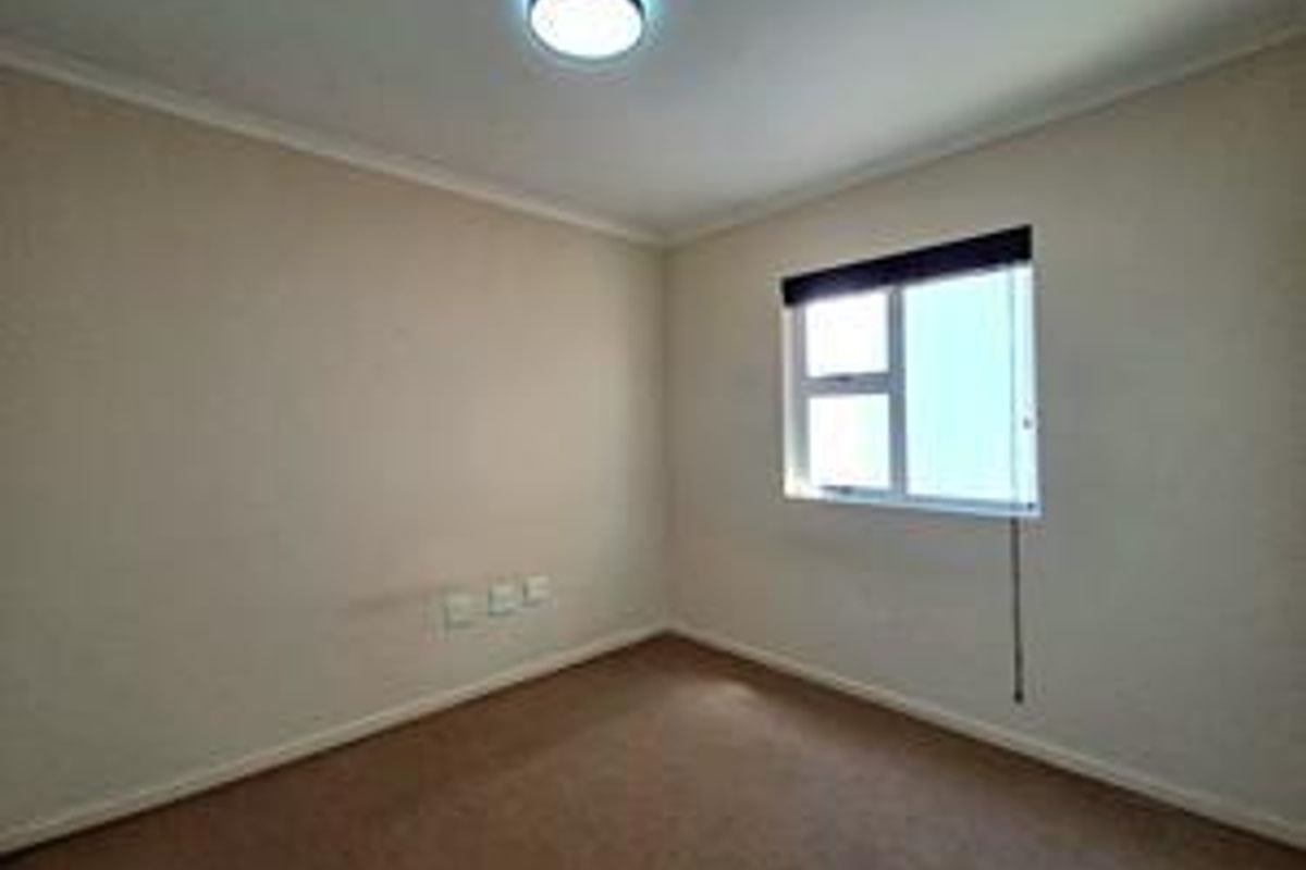 A clean, empty bedroom featuring neutral walls, carpeted flooring, and a functional sliding window with a fitted blind.