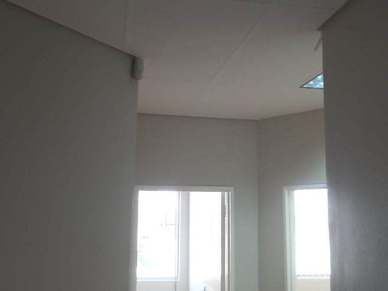 An empty office space featuring a suspended ceiling, recessed lighting, and a security sensor, providing a clean and functional work environment.