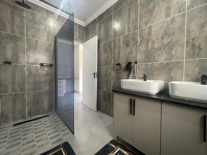 Modern bathroom featuring a spacious walk-in shower with glass screen, double vanity with vessel sinks, and contemporary grey tiled finishes.