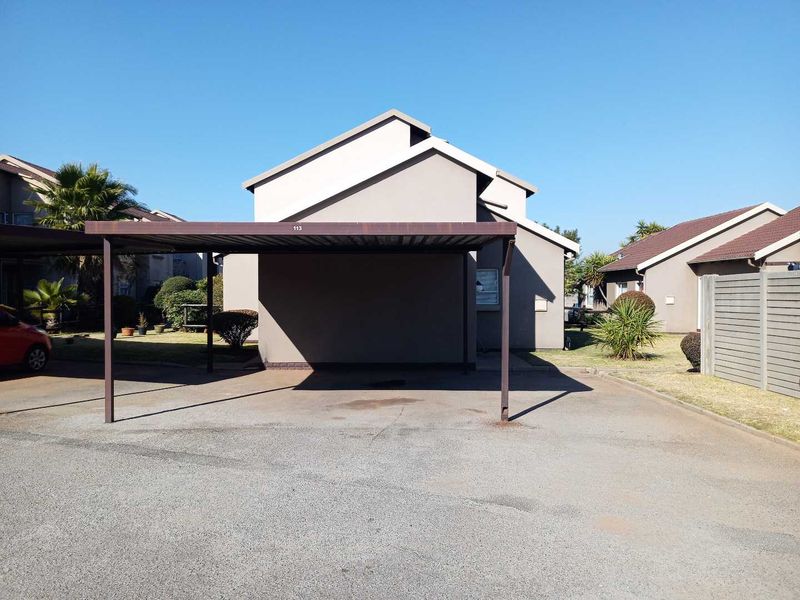 A dedicated carport structure providing covered parking, situated within a residential townhouse complex with paved driveway access.