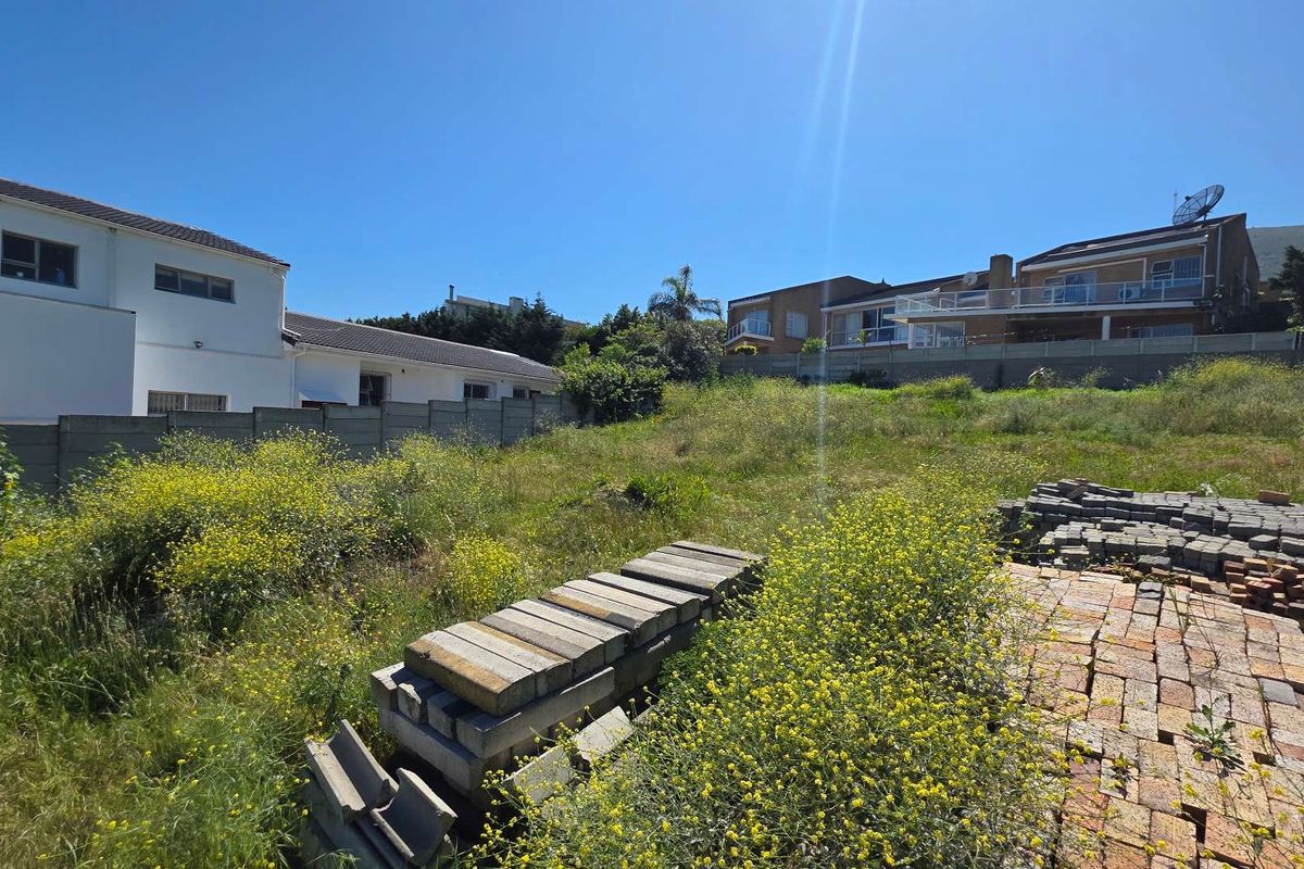 A vacant residential plot featuring overgrown vegetation, scattered paving bricks, and concrete boundary walls, situated in a developed neighborhood.