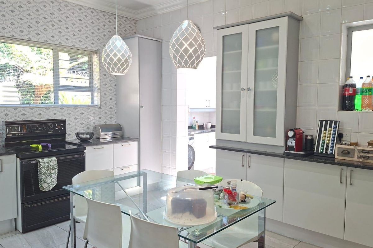 A bright, well-maintained kitchen featuring white cabinetry, stone countertops, a tiled backsplash, and a dedicated dining area with modern pendant lighting.