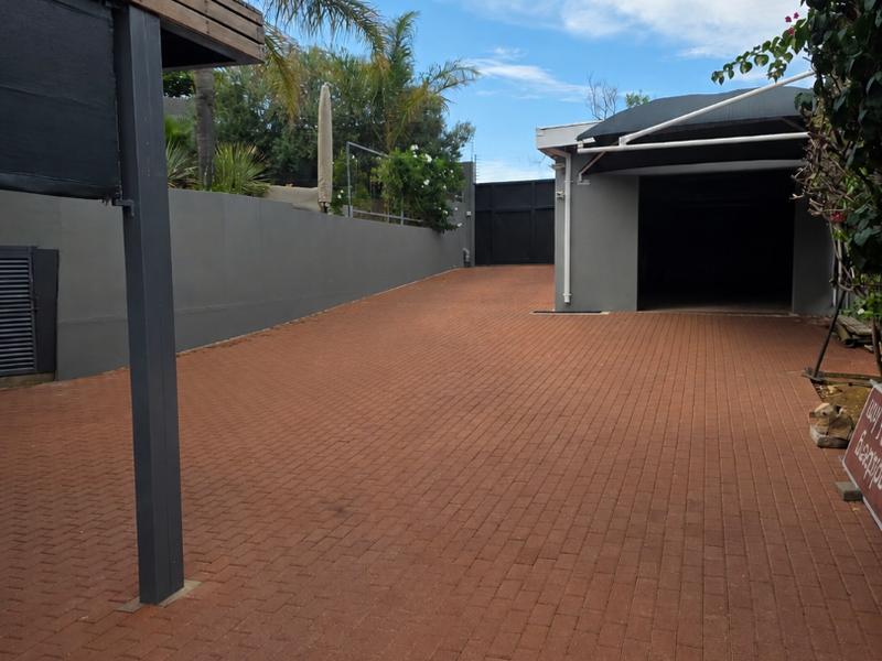 A well-maintained paved driveway leading to a garage, featuring a modern retaining wall and an elevated timber deck structure.