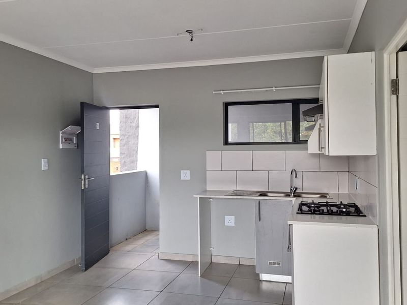 A clean, modern kitchen area featuring built-in cabinetry, a gas hob, stainless steel sink, and neutral tiled flooring in an open-plan layout.