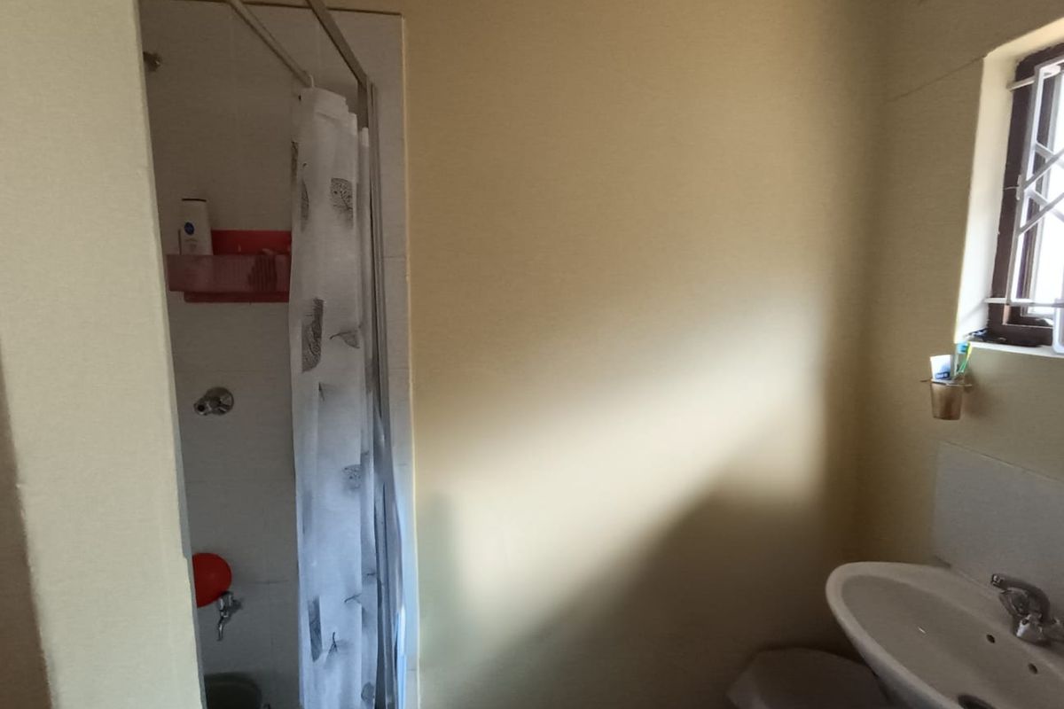 A functional bathroom featuring a shower enclosure and a pedestal basin, with security bars installed on the window.