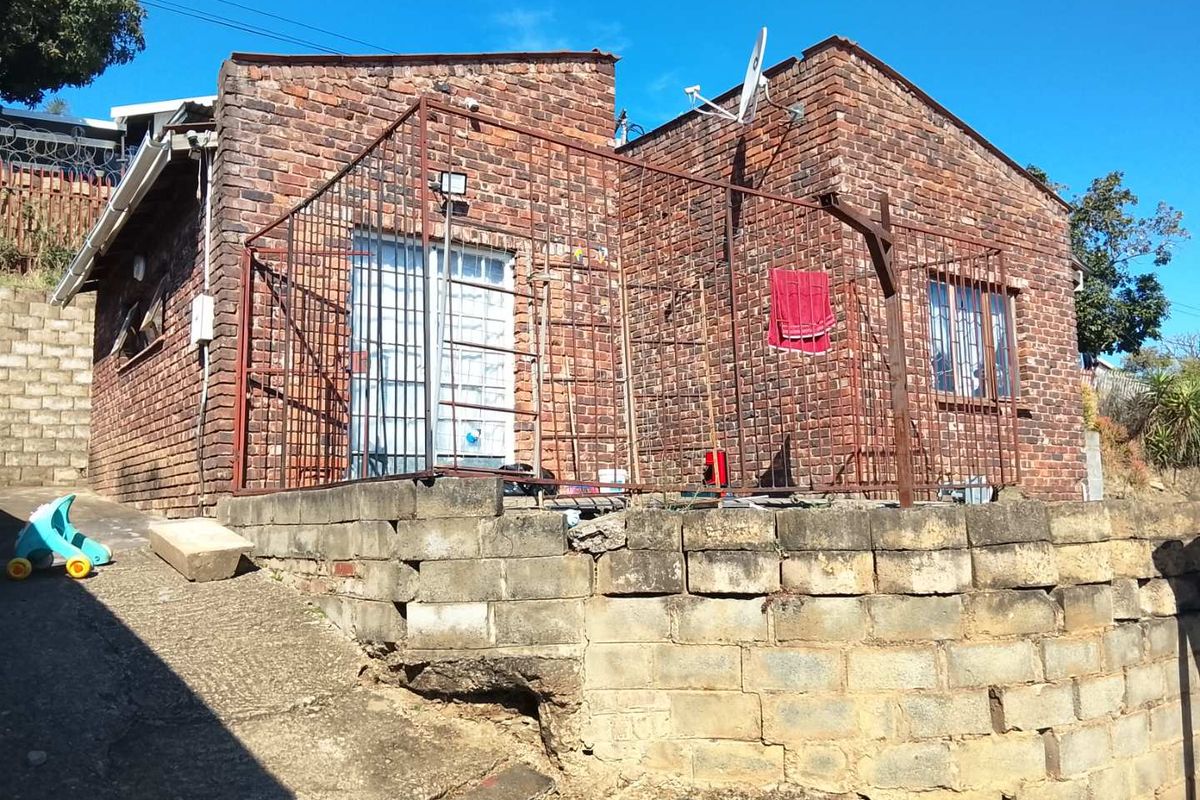 Rear view of a face brick house featuring a concrete retaining wall with visible structural erosion and security bars on windows and doors.