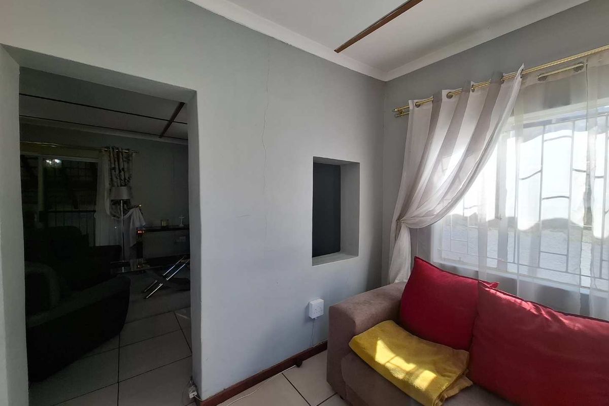 A living area featuring tiled flooring, a built-in wall niche, and a large window with security bars, connecting to an adjacent room.