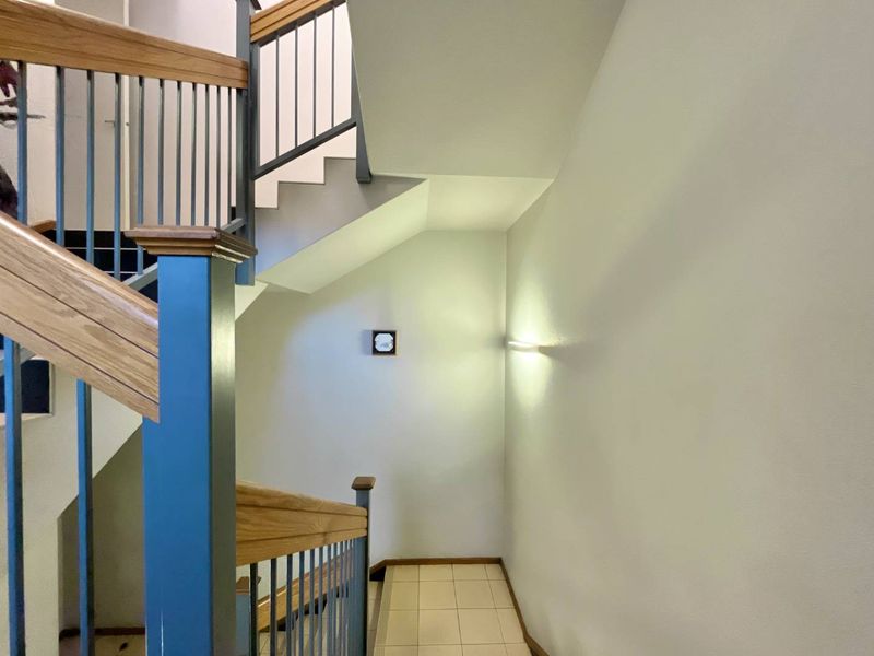 A clean and well-maintained office stairwell featuring a wooden handrail, metal balustrades, and tiled flooring with modern wall-mounted lighting.