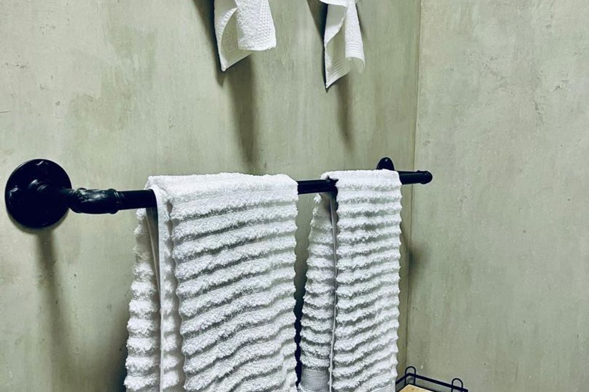 A modern bathroom detail featuring a black industrial-style towel rail and wall hooks mounted against a contemporary cement-finish wall.