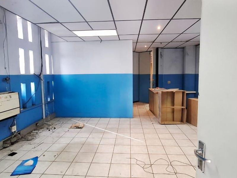 An empty office space featuring tiled flooring, a suspended ceiling, and a wall-mounted air conditioning unit, requiring cosmetic updates and repairs.