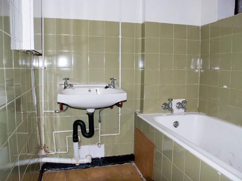 A dated bathroom featuring a wall-mounted basin and built-in bathtub with olive green wall tiling, requiring modernization and cosmetic updates.