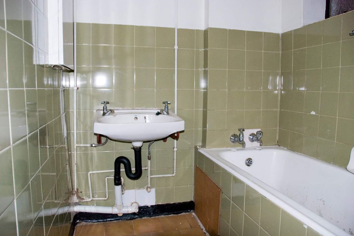 A dated bathroom featuring a wall-mounted basin and built-in bathtub with olive green wall tiling, requiring modernization and cosmetic updates.