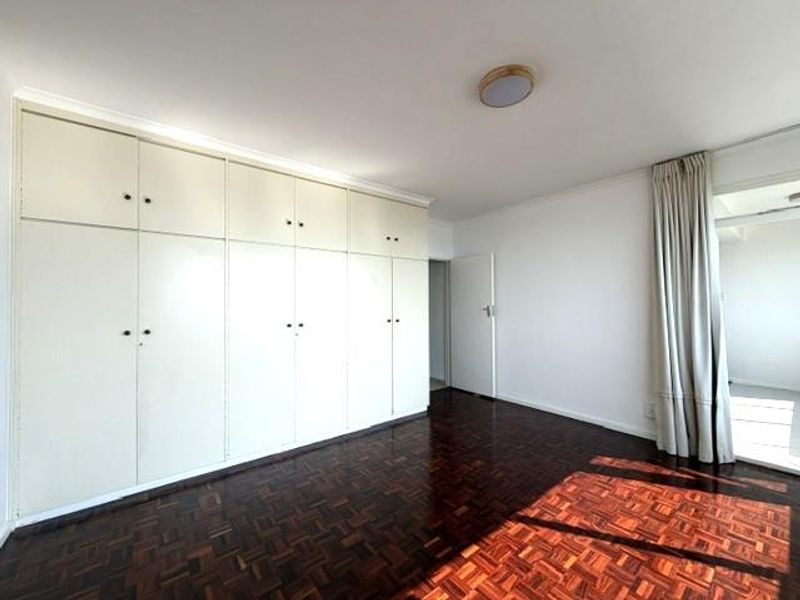 Spacious bedroom featuring classic parquet flooring and extensive built-in cupboard storage, offering a clean and neutral canvas for personalization.