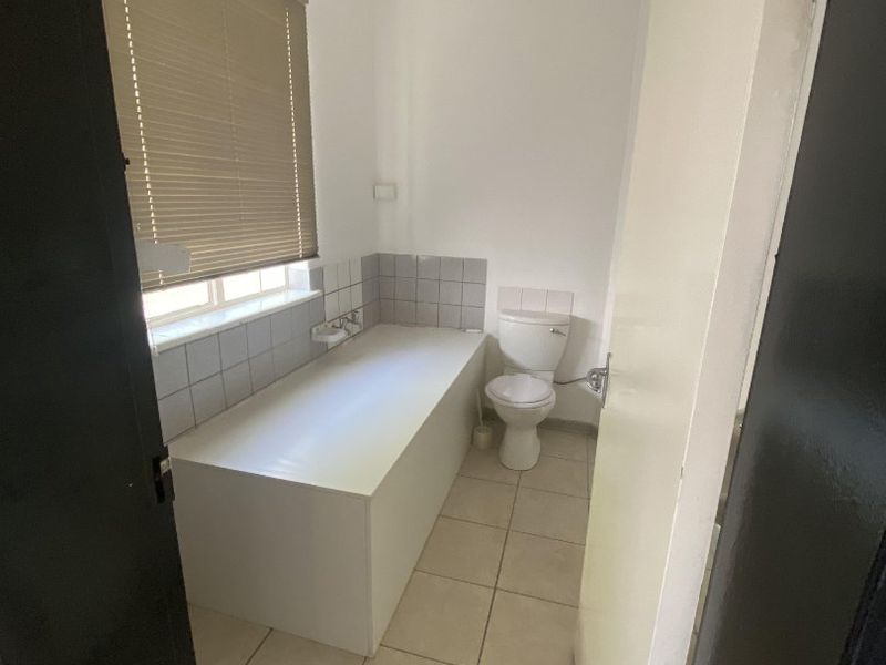 A functional bathroom featuring a built-in bathtub, toilet, and neutral tiled flooring with a tiled splashback.