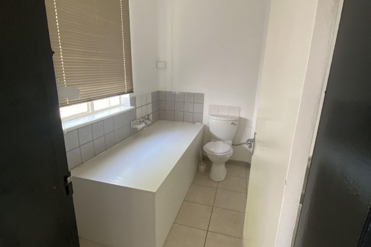 A functional bathroom featuring a built-in bathtub, toilet, and neutral tiled flooring with a tiled splashback.