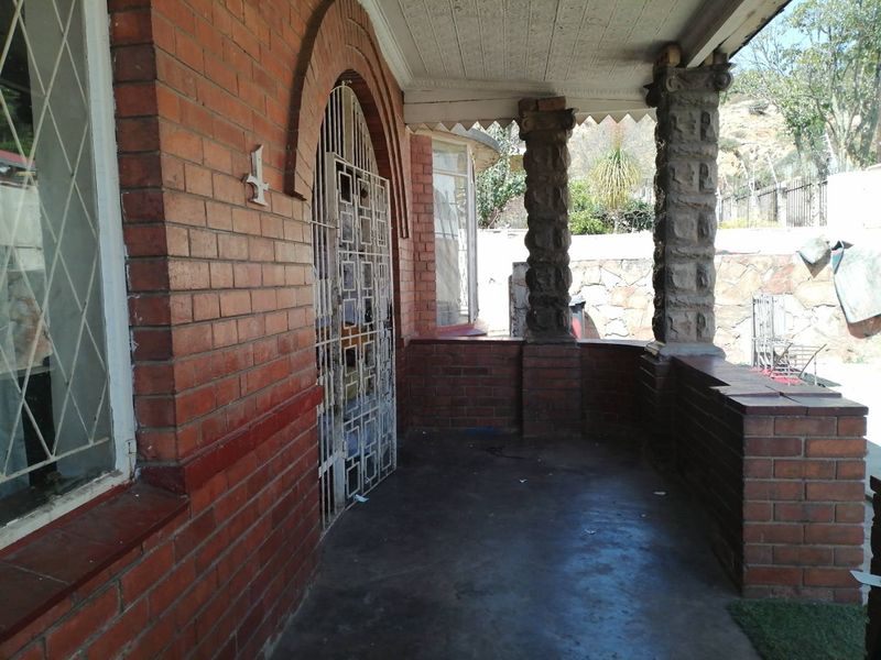 Covered front patio featuring classic brickwork, stone columns, and a secure metal gate entrance.