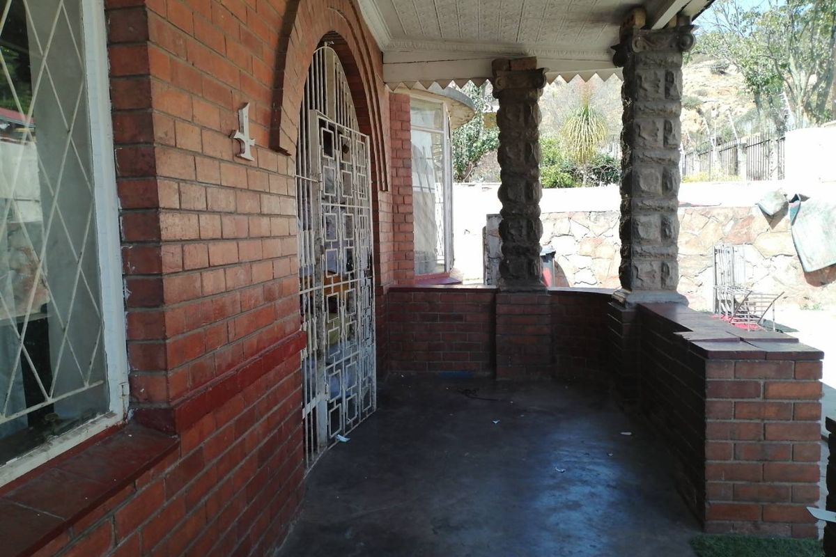 Covered front patio featuring classic brickwork, stone columns, and a secure metal gate entrance.