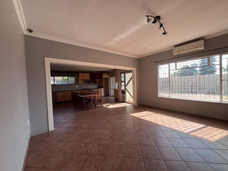 Spacious open-plan living and kitchen area featuring tiled flooring, air conditioning, and large windows with security bars.
