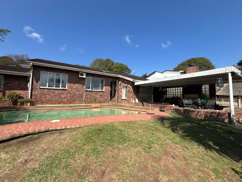 Rear exterior view featuring a swimming pool, brick patio area, and a covered outdoor entertainment space with a built-in brick chimney.