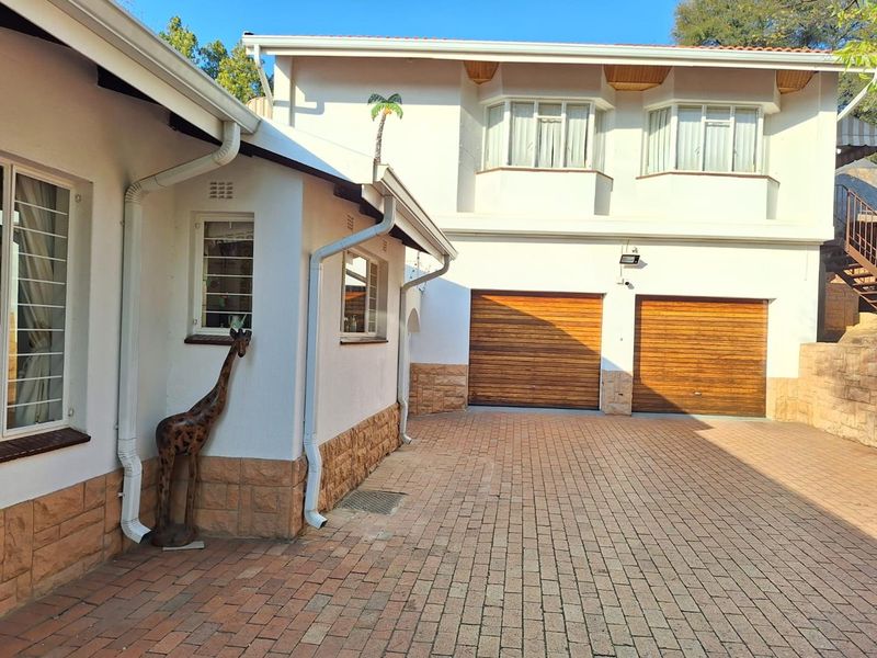 A well-maintained exterior view of the property featuring a paved driveway, double garage with wooden doors, and stone-clad base detailing.