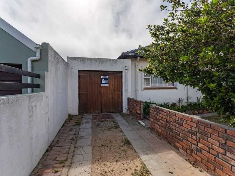 Front exterior view featuring a wooden garage door, brick boundary wall, and paved driveway access.