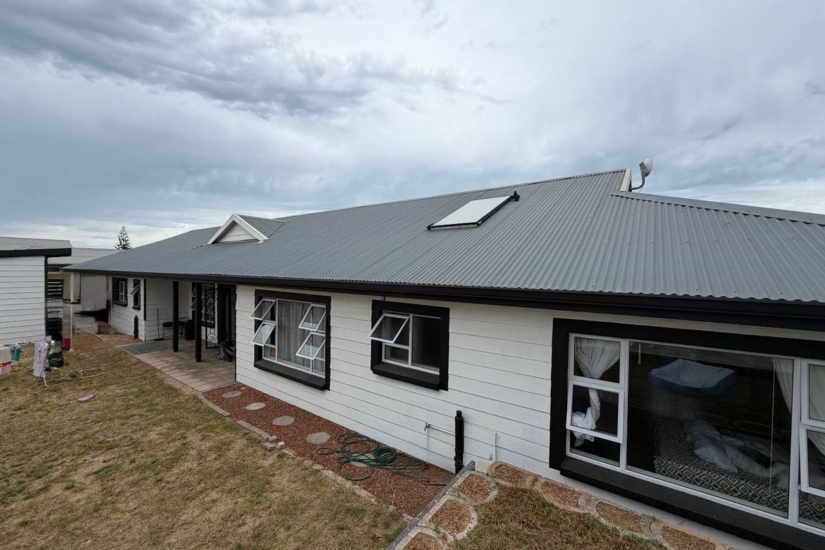 Rear view of the house featuring a corrugated metal roof, white weatherboard cladding, dark window frames, and a paved patio area.