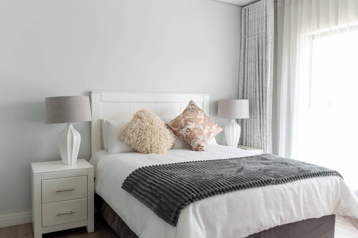 A bright and well-maintained bedroom featuring neutral wall finishes, floor-to-ceiling curtains, and ample natural light.