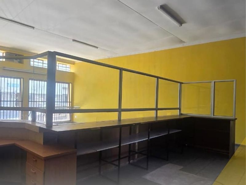 An empty office space featuring a built-in reception counter with a glass partition, fluorescent lighting, and security bars on the windows.